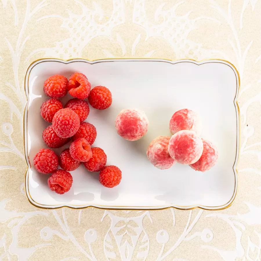 DORNAUERS Grand Cru Pralinen Himbeere, angerichtet neben frischen Himbeeren auf einem weißen Porzellanteller mit goldener Verzierung