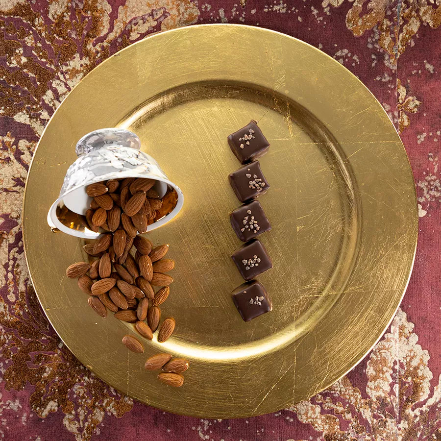 DORNAUERS Grand Cru Pralinen Baumnuss auf goldenem Teller, daneben eine umgekippte Tasse mit ganzen Mandeln 