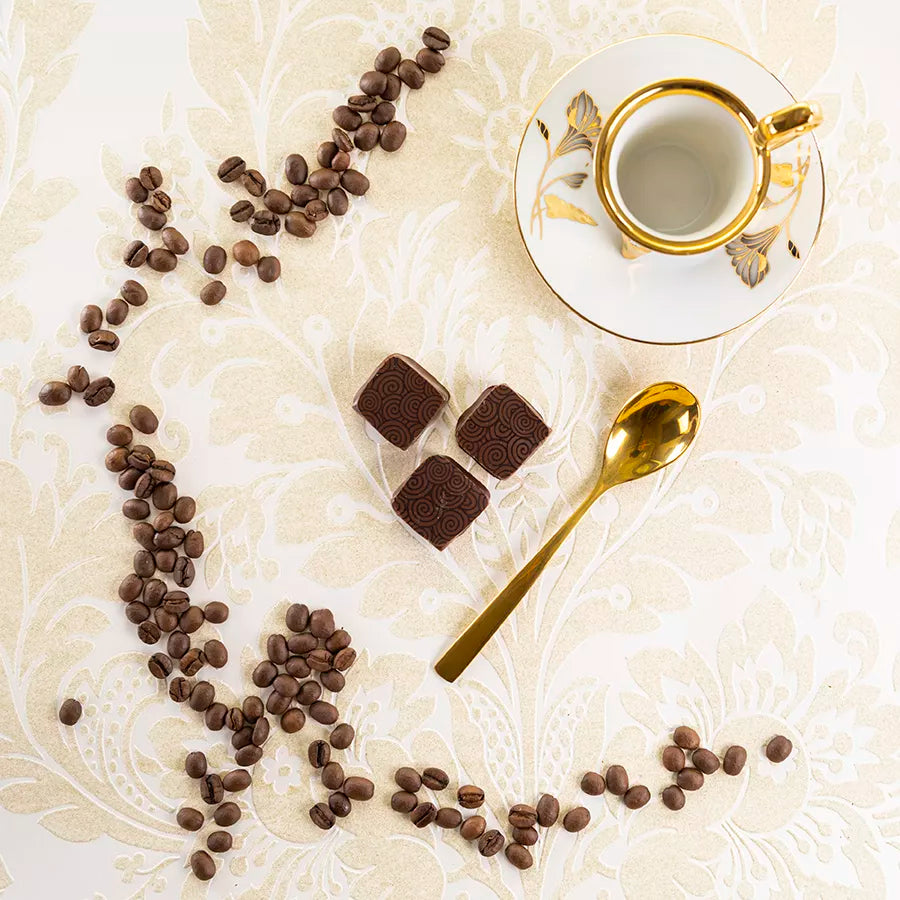 DORNAUERS Grand Cru Pralinen Kaffee Nougat, umgeben von Kaffeebohnen, goldener Espressotasse und Löffel