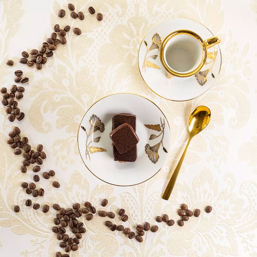 DORNAUERS Grand Cru Pralinen Kaffee Nougat auf weißem Teller, umgeben von Kaffeebohnen, goldener Espressotasse und Löffel