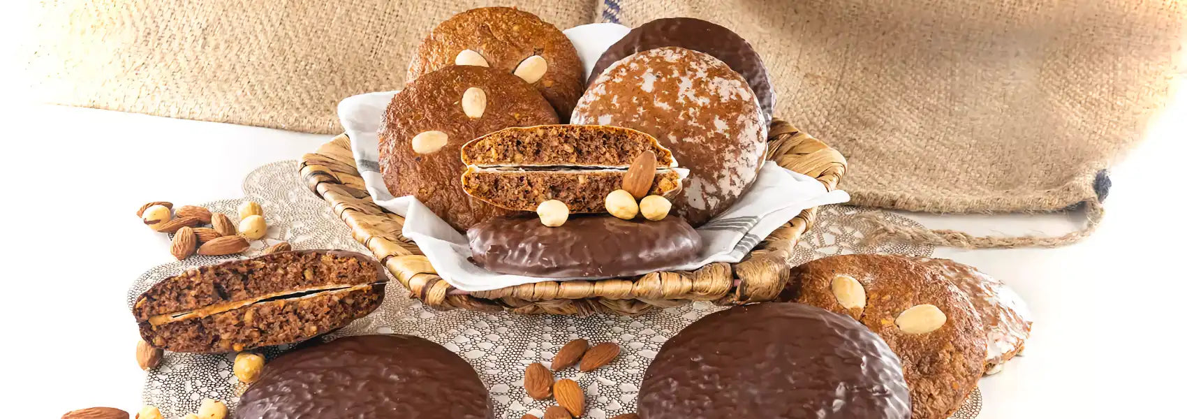 Dornauers Elisenlebkuchen in einem Korb, in drei Sorten: schokolade, süß glasiert oder natur – umgeben von ganzen Mandeln und Haselnüssen.