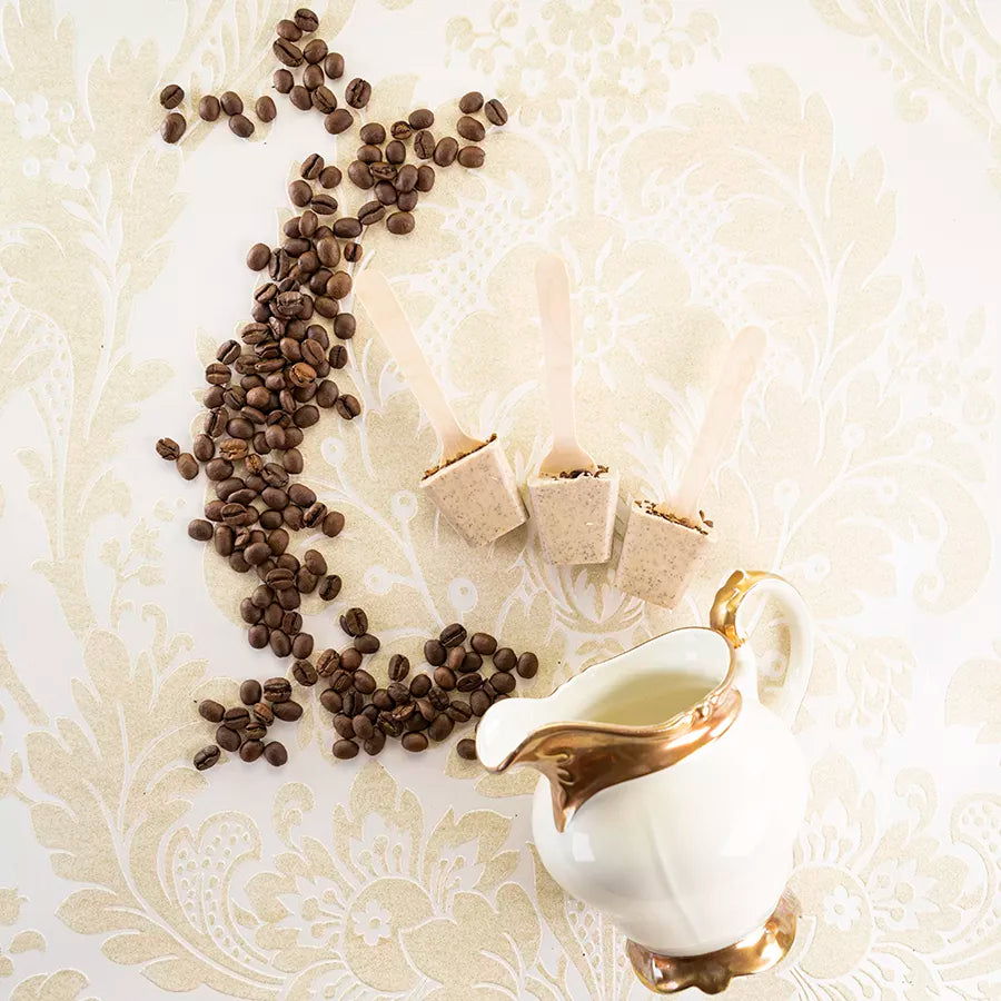 DORNAUERS Trinkschokolade Kaffee am Stiel, daneben Kaffeebohnen und eine weiße Porzellan Kanne mit Goldrand