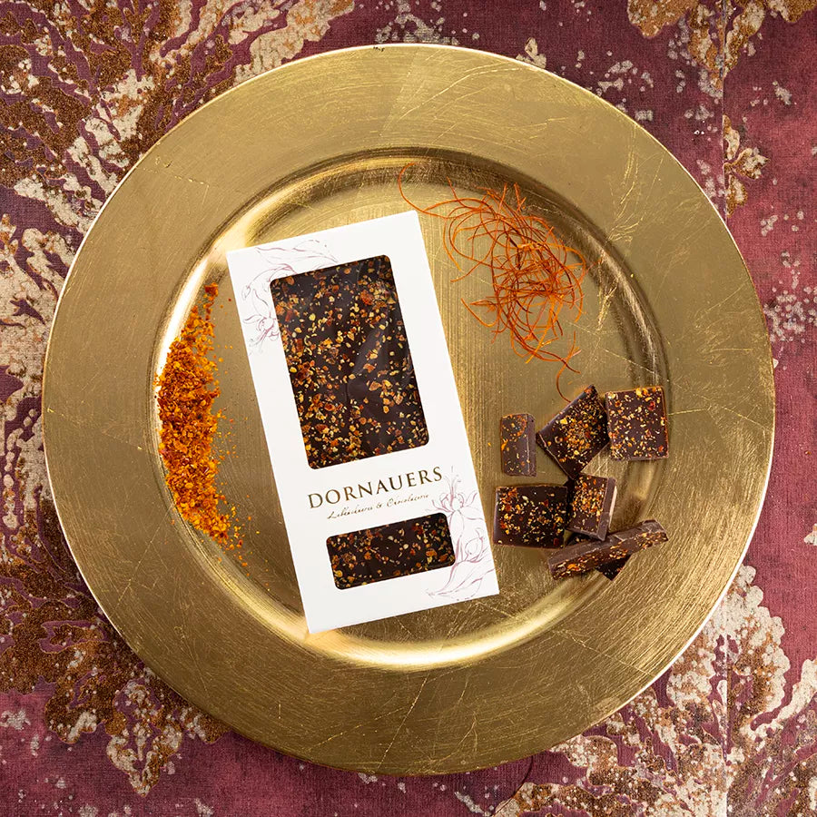 DORNAUERS Grand Cru Schokolade Chili auf goldenem Teller, dekoriert mit der Verpackung, Chilipulver und Chilifäden