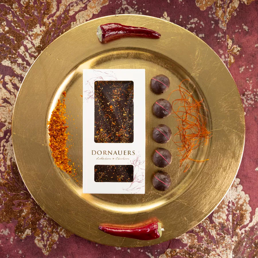DORNAUERS Grand Cru Schokolade Chili auf goldenem Teller, dekoriert mit Chilischoten, Chilipulver, Chilifäden und Grand Cru Chili Pralinen 