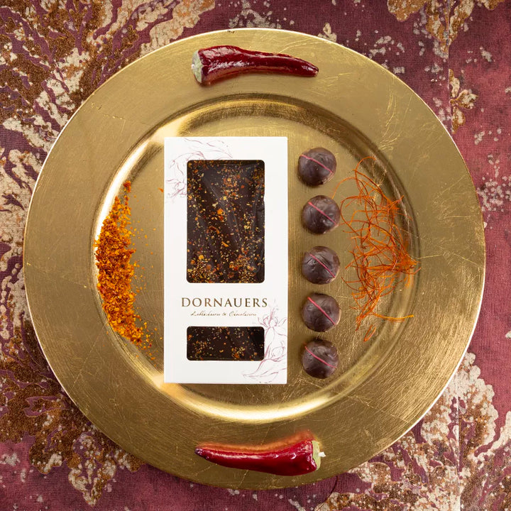 DORNAUERS Grand Cru Schokolade Chili auf goldenem Teller, dekoriert mit Chilischoten, Chilipulver, Chilifäden und Grand Cru Chili Pralinen 