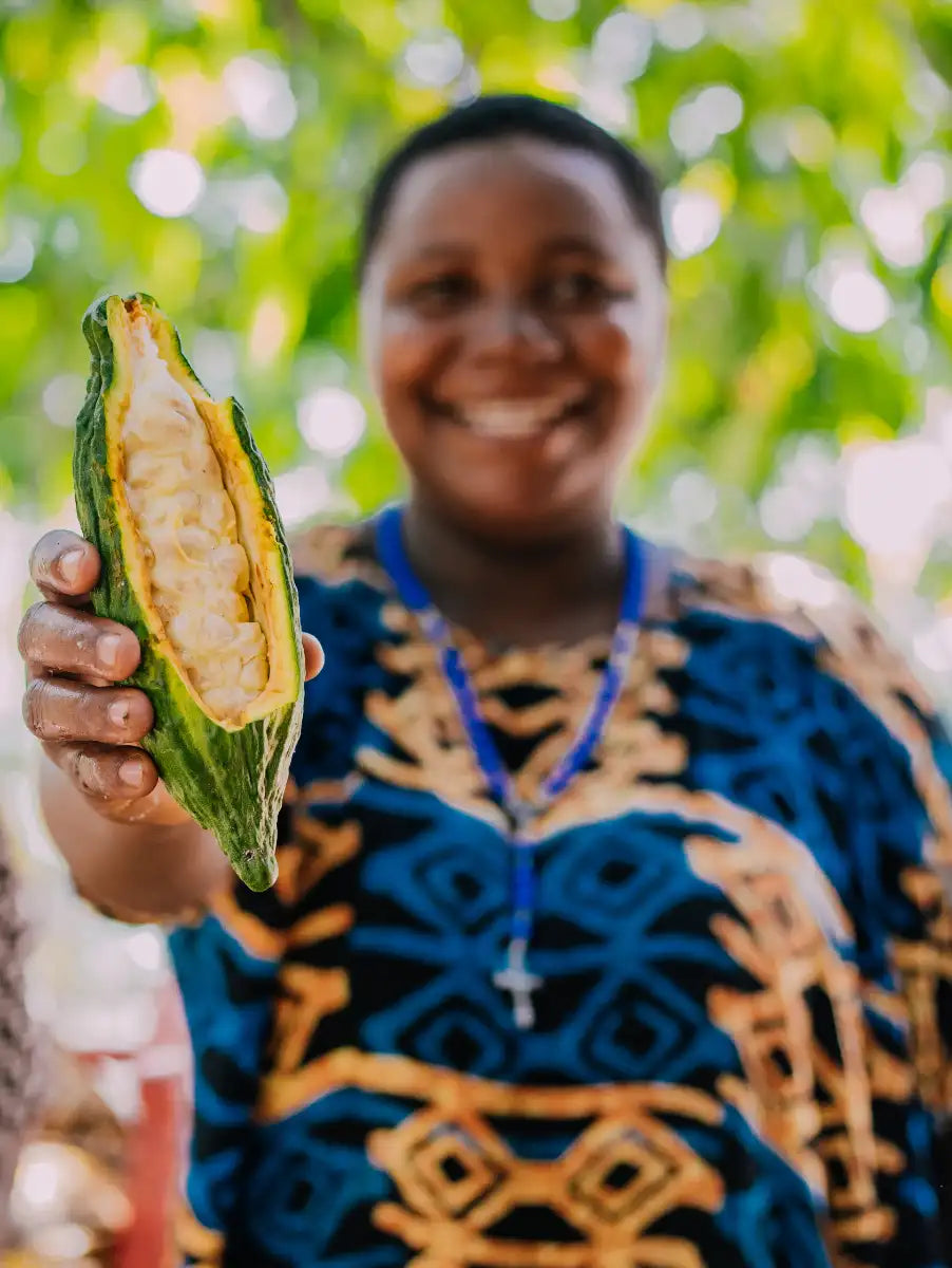 Lächelnde Frau zeigt eine aufgeschnittene Kakaofrucht mit weißen Kakaobohnen – Nahaufnahme des Ursprungs der Schokolade.
