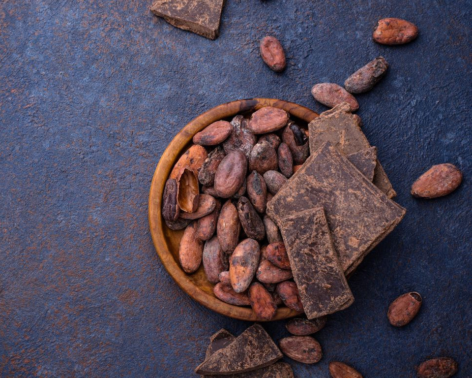 Holzteller mit Kakaobohnen und grob gebrochener dunkler Schokolade auf rustikalem Hintergrund